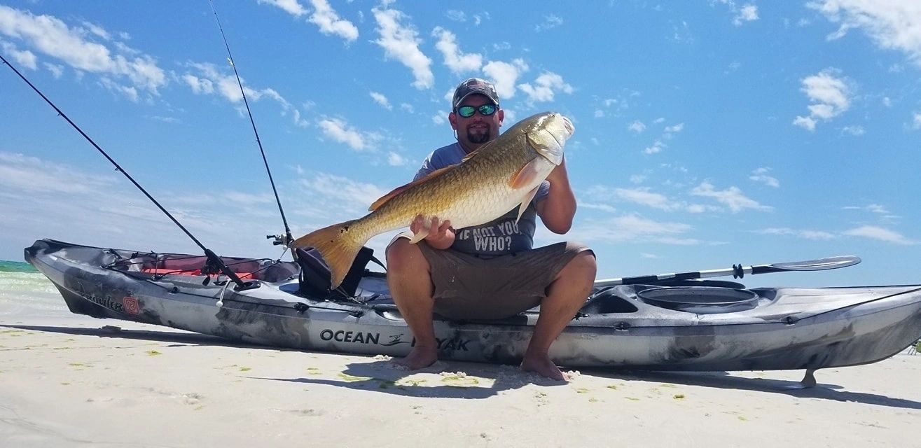 A guest holding up a redfish caught from an Ocean Kayak Prowler on the beach