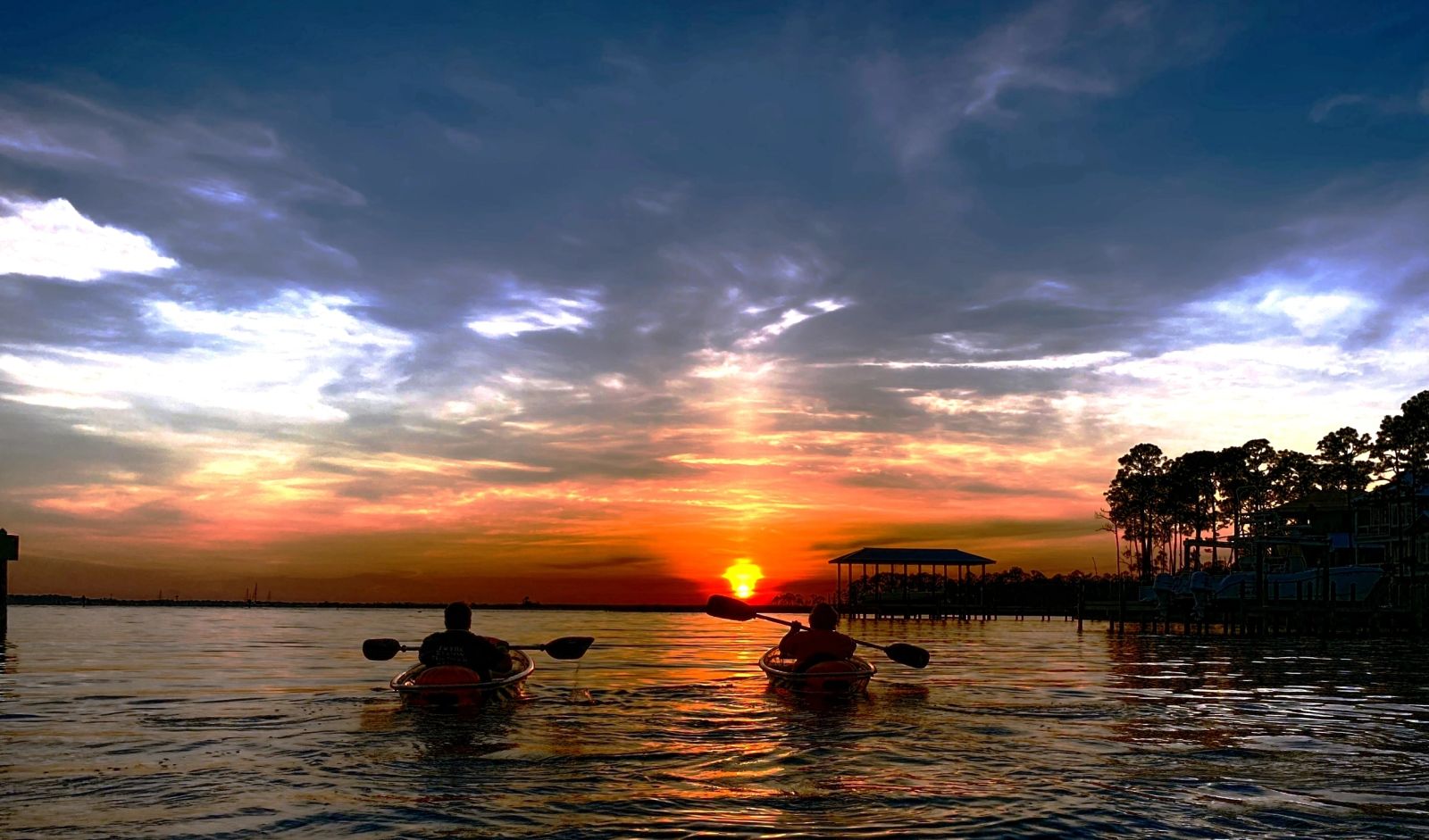 Two paddlers silhouetted against a sunset over Destin Harbor