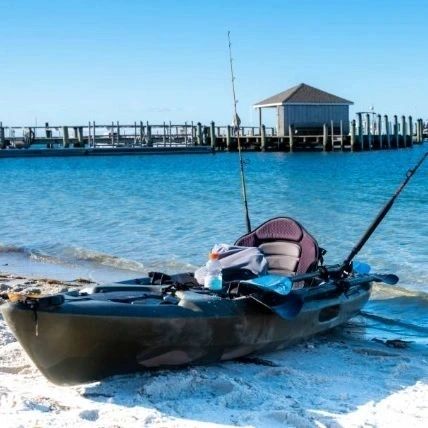 A fishing kayak beached on white sand near a boat dock in clear shallow water